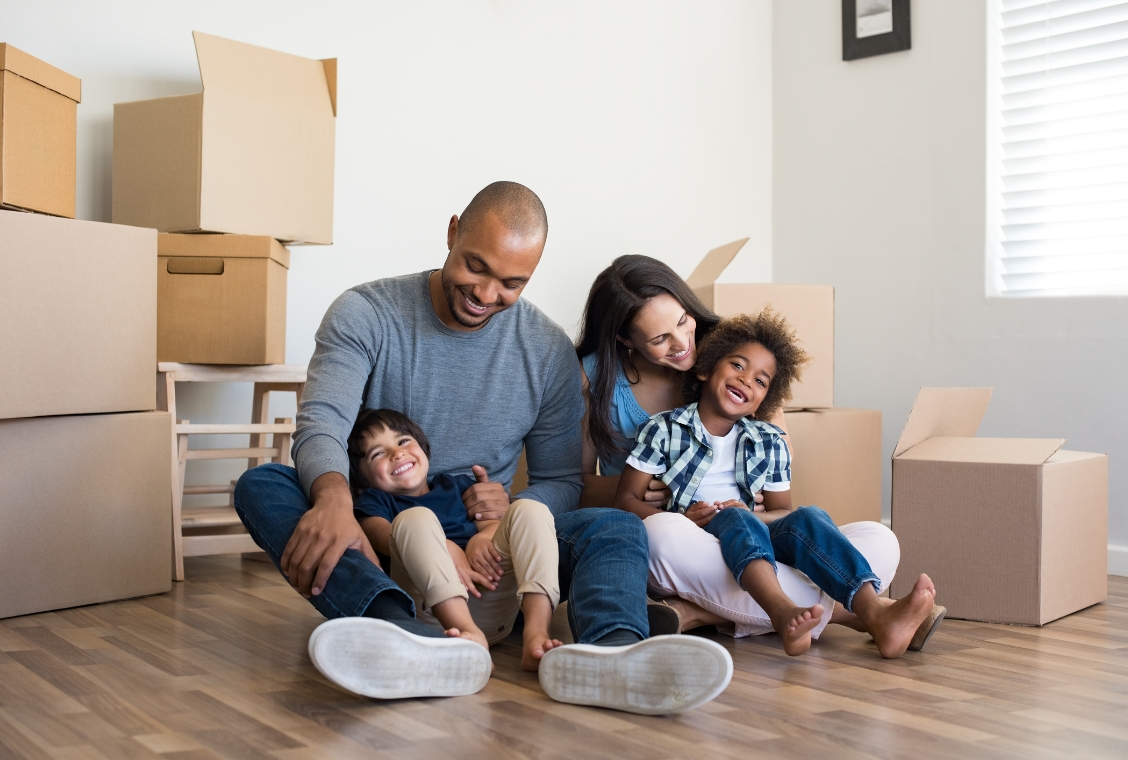 Family sitting on floor of house with boxes around them.