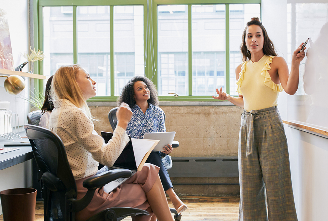 Woman looking to whiteboard in a meeting with a diverse female team.