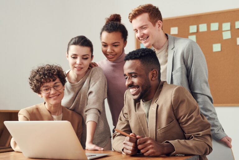 A group of people all leaning over a laptop screen.