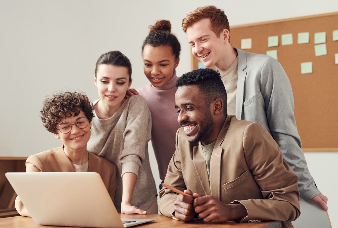 A group of people all leaning over a laptop screen.